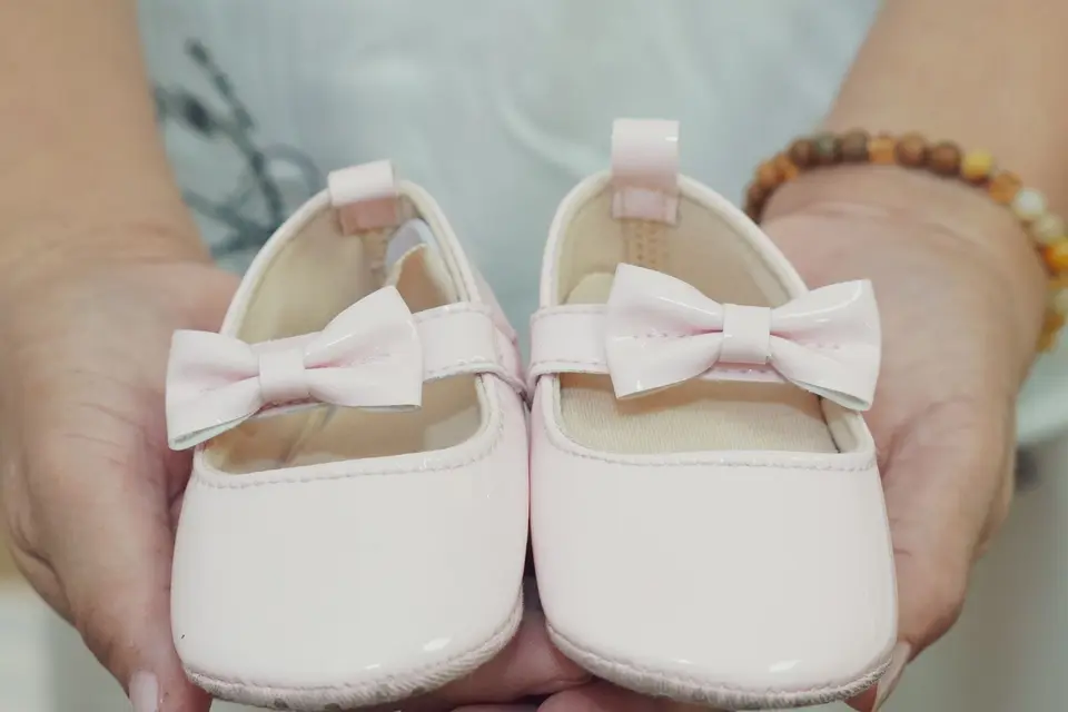 Primer plano de unas manos que sujetan unos zapatitos blancos de bebé con lazo