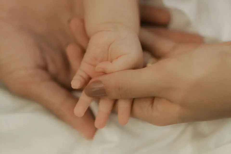 Manos de adultos sostienen la mano de un bebé sobre una tela blanca