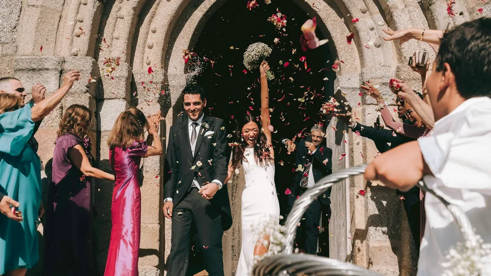 Los novios salen de la iglesia mientras los invitados les lanzan pétalos