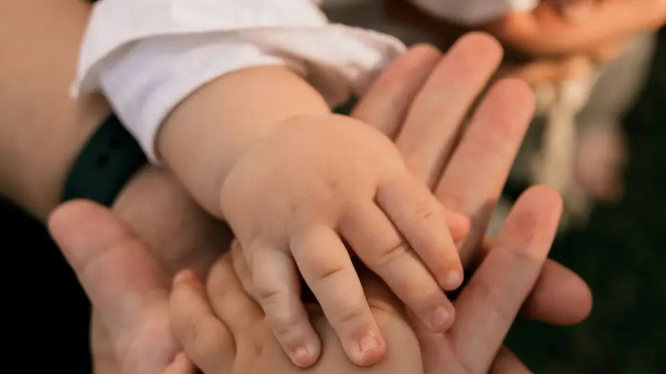 Primer plano de la mano de un bebé apoyada sobre varias manos adultas