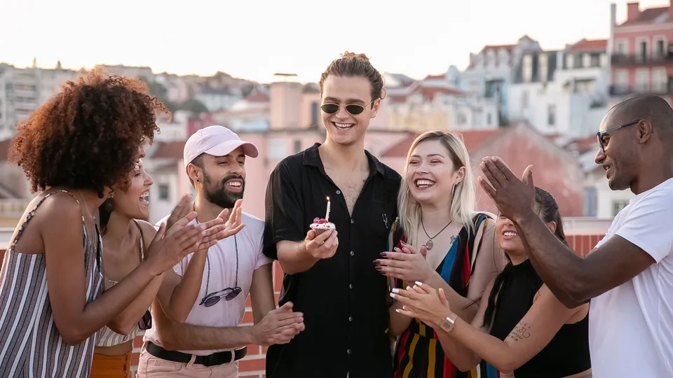 Un grupo de amigos aplaude a un chico que sostiene una magdalena con una vela en una azotea de Lisboa