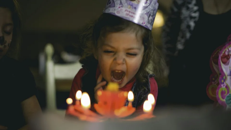 Una niña con corona de cumpleaños sopla las velas de su tarta