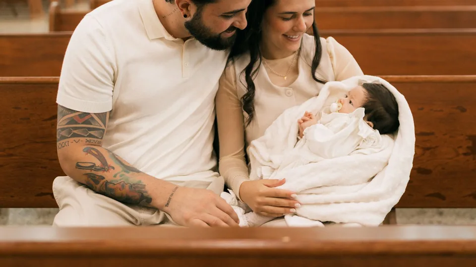 Unos padres sostienen a su bebé en un banco de la iglesia el día del bautizo