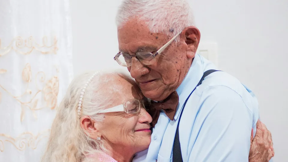 Una pareja mayor se abraza con los ojos cerrados junto a la tarta de su aniversario