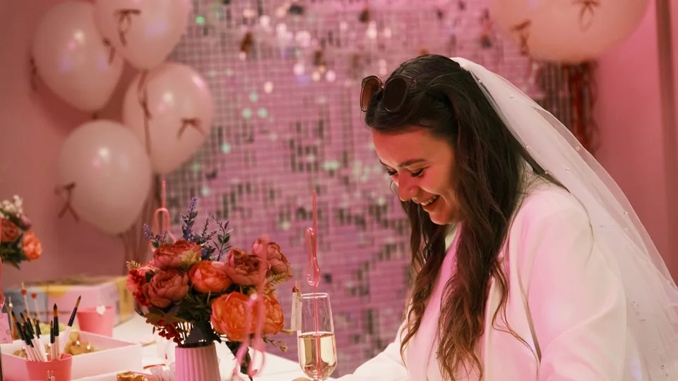 La futura novia, con velo, ríe en su despedida de soltera junto a flores y copas de cava