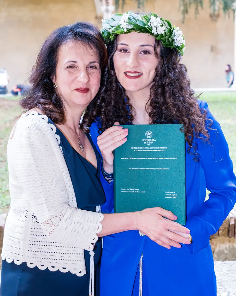 Una graduada con corona de laurel y su madre posan con el título el día de la graduación