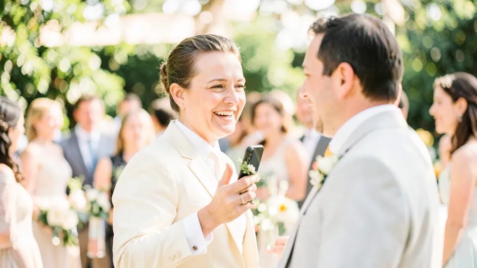 Invitada sonriendo con el móvil en la mano durante un cóctel de boda al aire libre