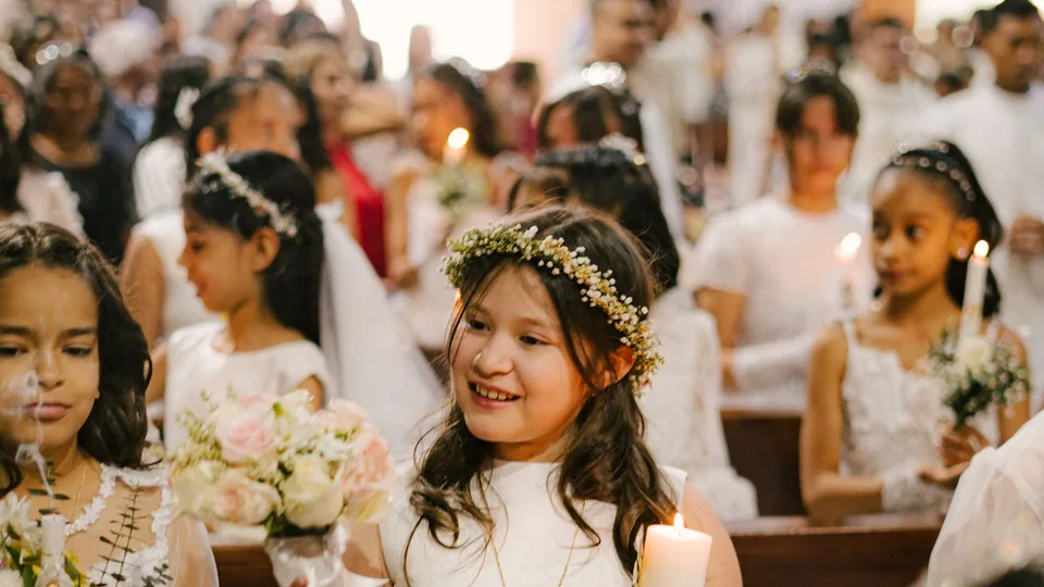 Niñas vestidas de primera comunión con velas y ramos en los bancos de la iglesia durante la ceremonia