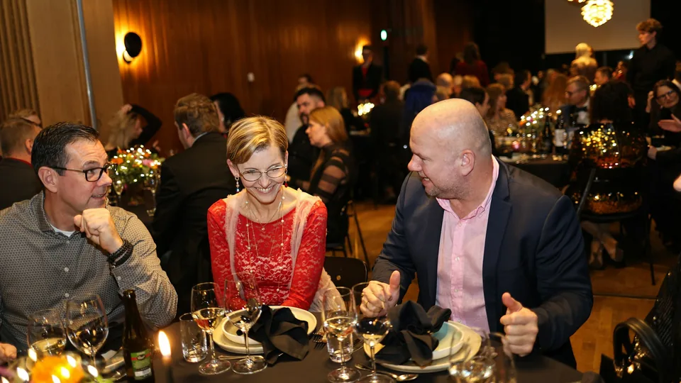 Invitados conversan y ríen sentados a la mesa durante una cena de celebración
