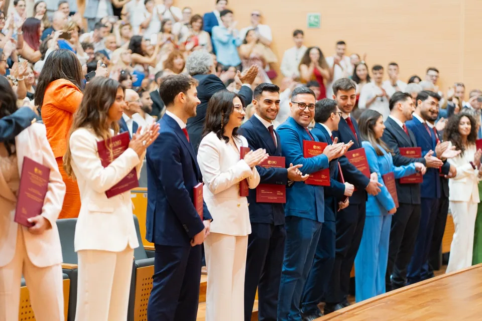 Graduados de pie aplauden con sus títulos durante la ceremonia de graduación