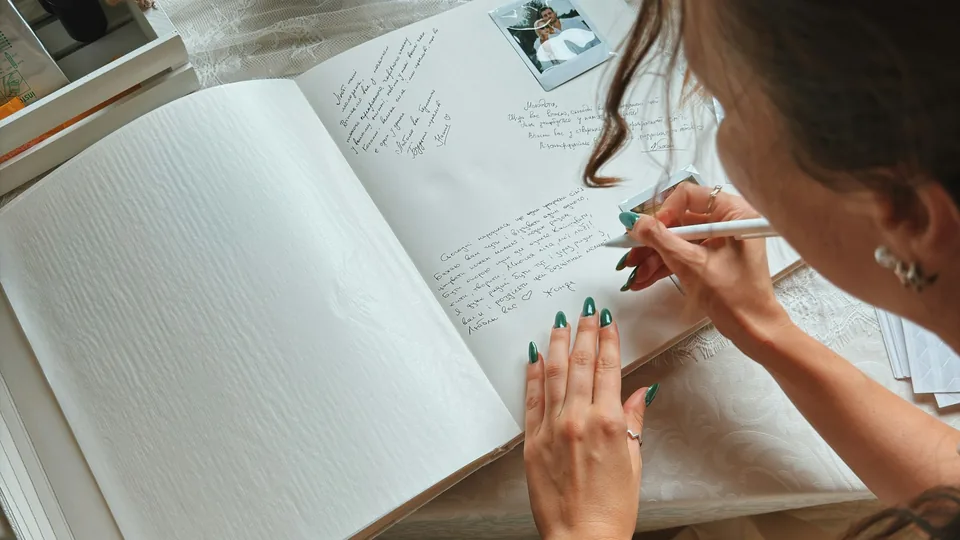 Una invitada escribe un mensaje en el libro de firmas de una boda, junto a fotos instantáneas