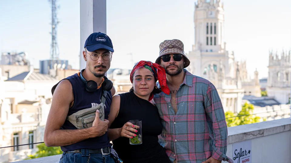 Tres amigos posan sonrientes en una azotea de Madrid con edificios históricos al fondo