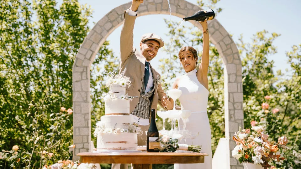 Los novios brindan con cava junto a la tarta en un jardín