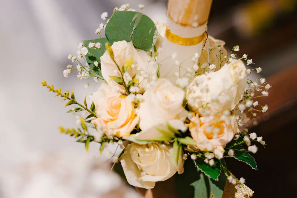 Un ramo de rosas claras sujeto a una vela de comunión, con un vestido blanco desenfocado detrás
