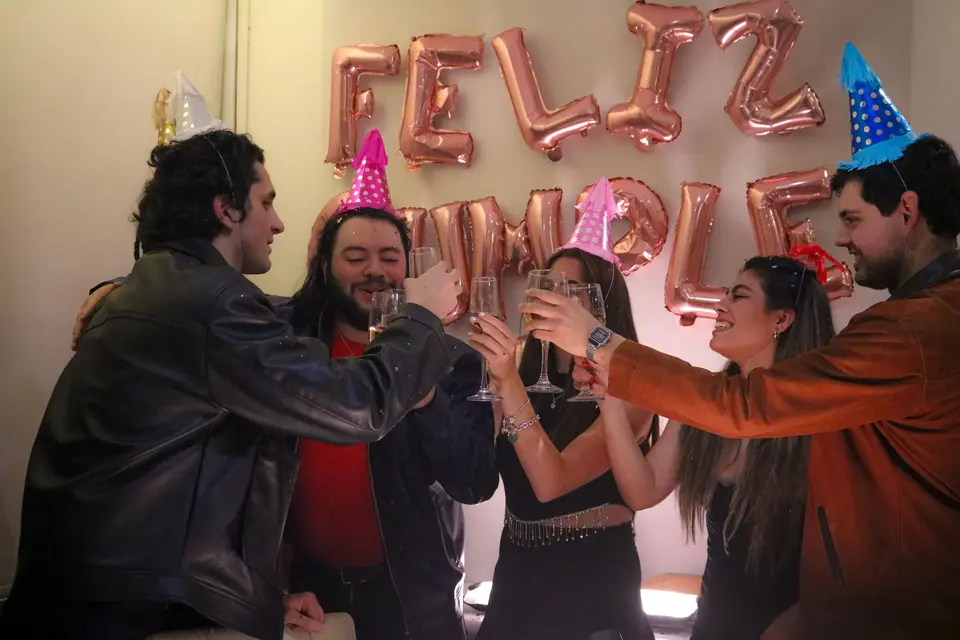 Cuatro amigos con gorros de fiesta chocan sus copas en el brindis de un cumpleaños