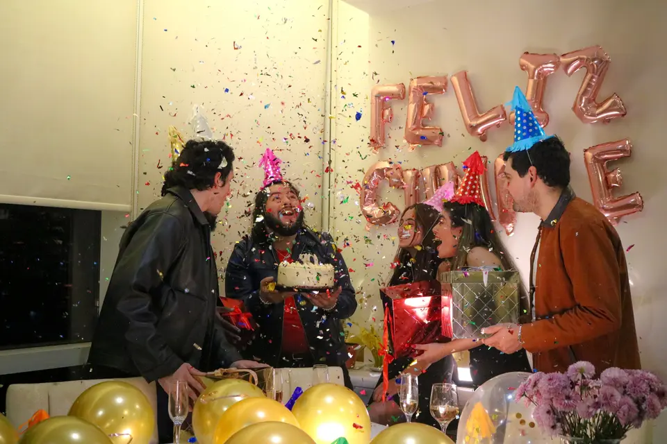 Un grupo de amigos con gorros de fiesta entrega la tarta de los 30 entre confeti, regalos y globos dorados