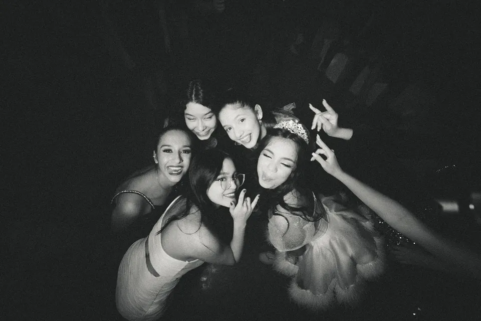Amigas posan juntas y riendo con la quinceañera, en blanco y negro