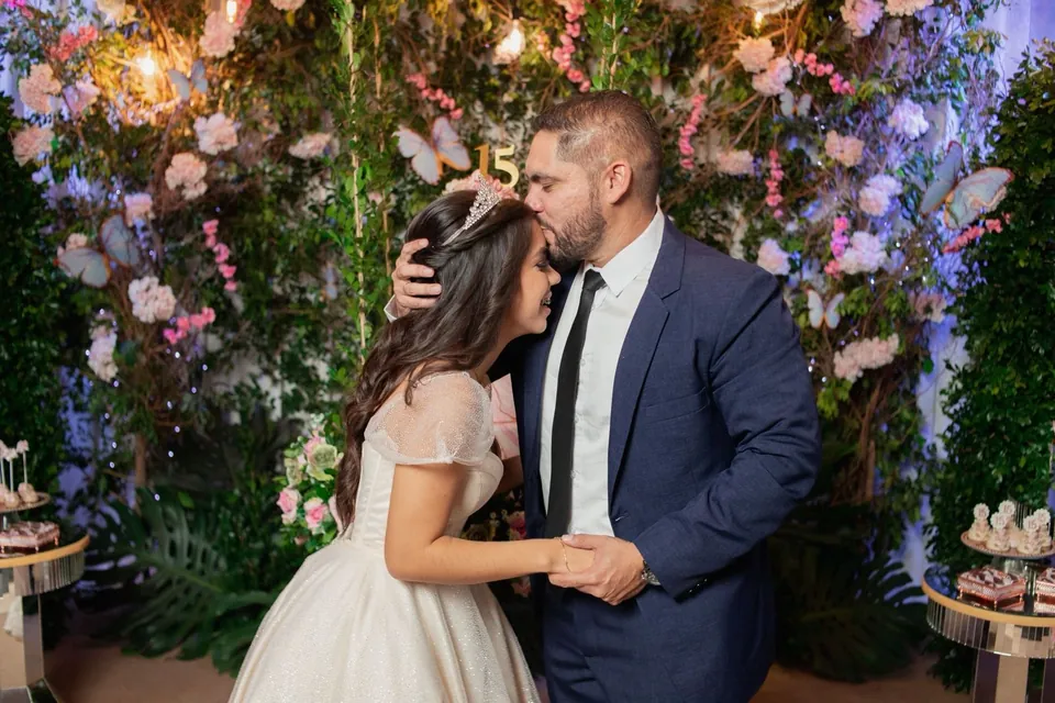 Un padre besa en la frente a su hija quinceañera entre flores