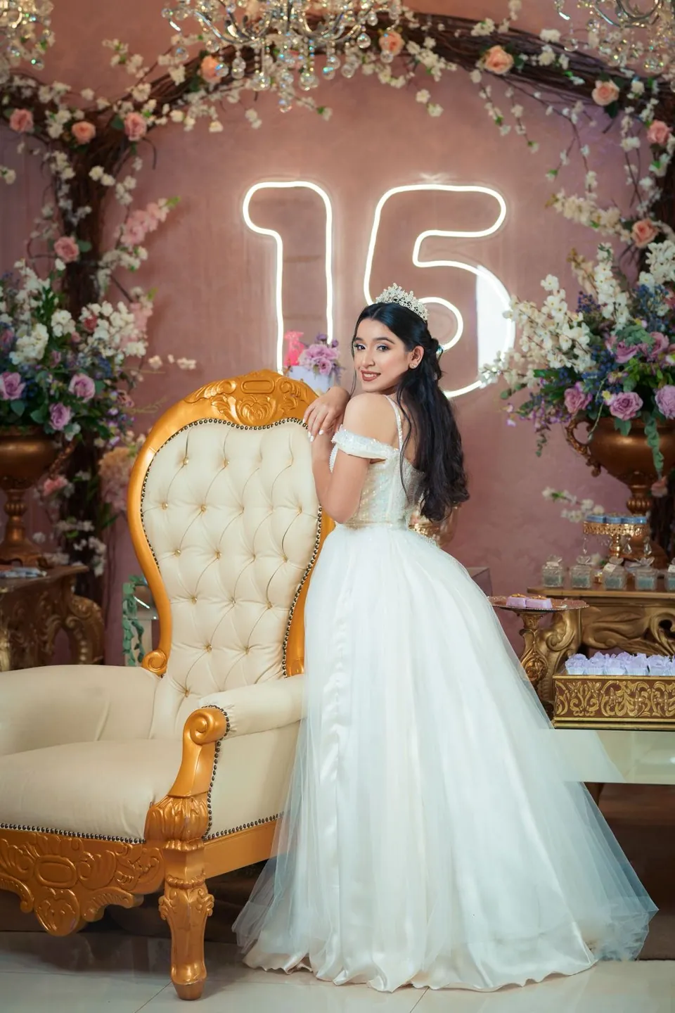 La quinceañera junto a un sillón dorado y un número 15 luminoso